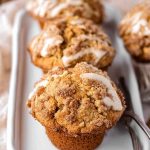 Golden Apple Butter Muffins with a crumbly streusel topping and a drizzle of white glaze, arranged on a white plate.