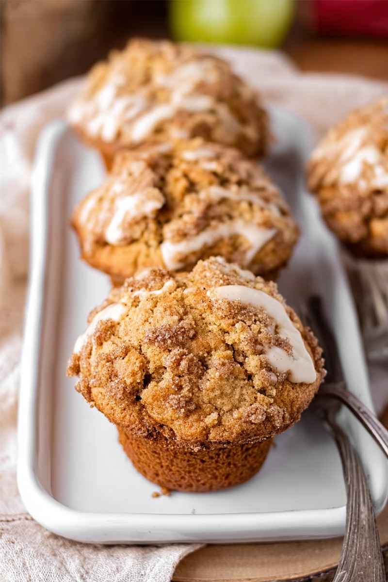 Golden Apple Butter Muffins with a crumbly streusel topping and a drizzle of white glaze, arranged on a white plate.