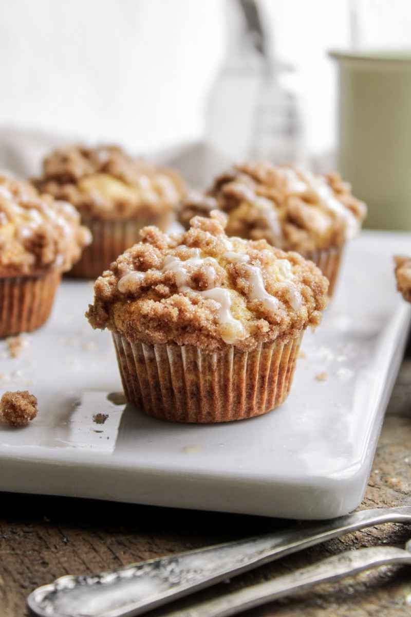 Delicious apple muffins with a golden streusel topping and a light glaze, displayed on a white marble serving tray.