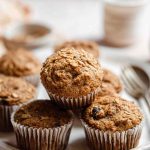 A plate of freshly baked applesauce muffins, some topped with oats, set against a warm, inviting backdrop with a cup of tea.
