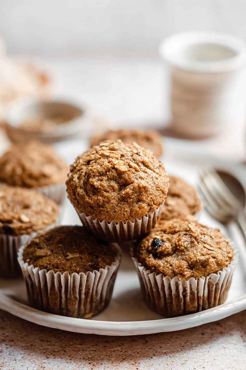 A plate of freshly baked applesauce muffins, some topped with oats, set against a warm, inviting backdrop with a cup of tea.
