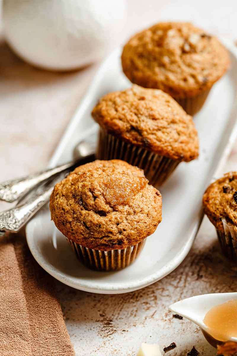 A plate of golden-brown applesauce muffins with raisins, served on white paper liners, accompanied by a cup of tea.