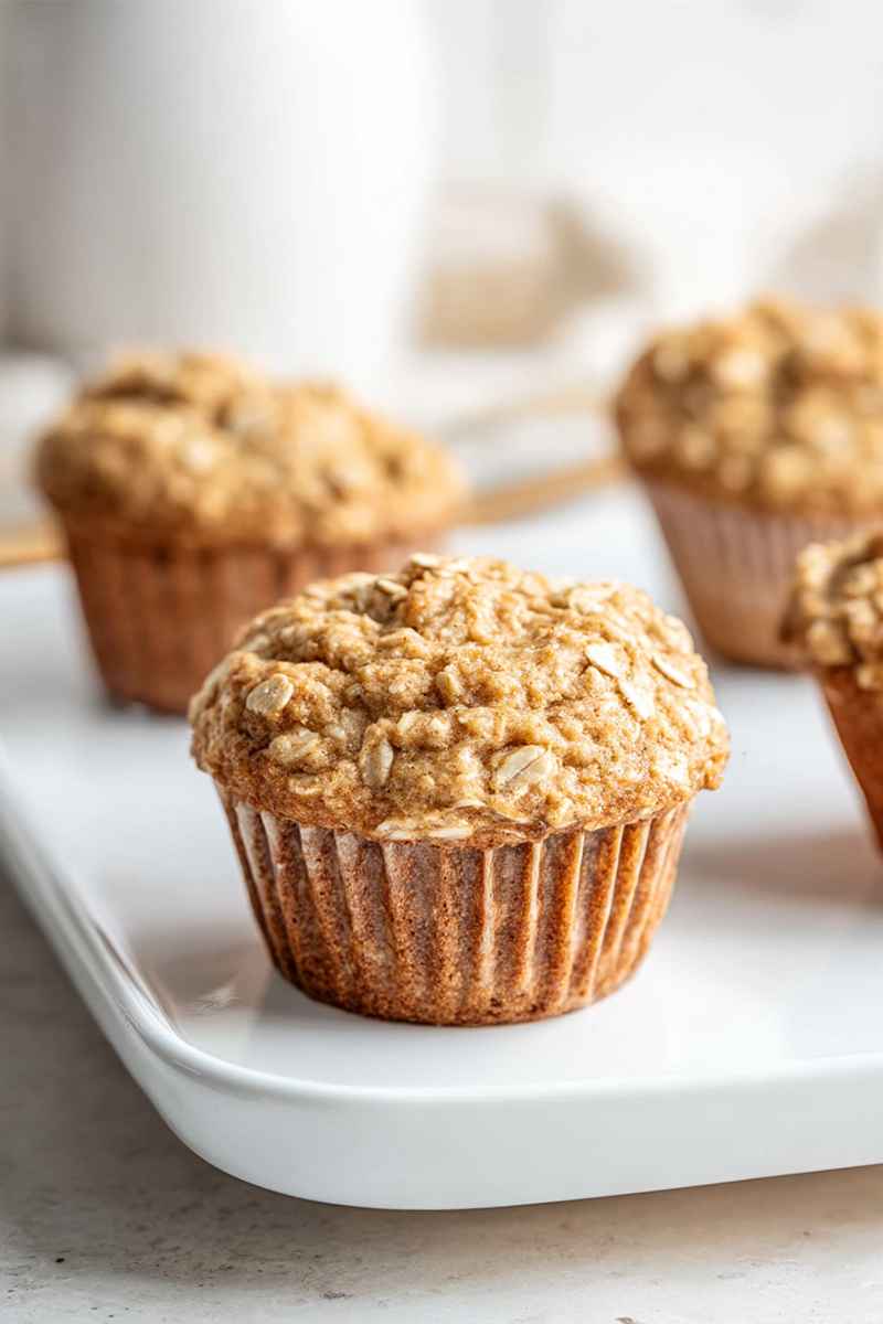 Golden applesauce oatmeal muffins with a sprinkle of oats, arranged on a white tray, ready to be enjoyed.
