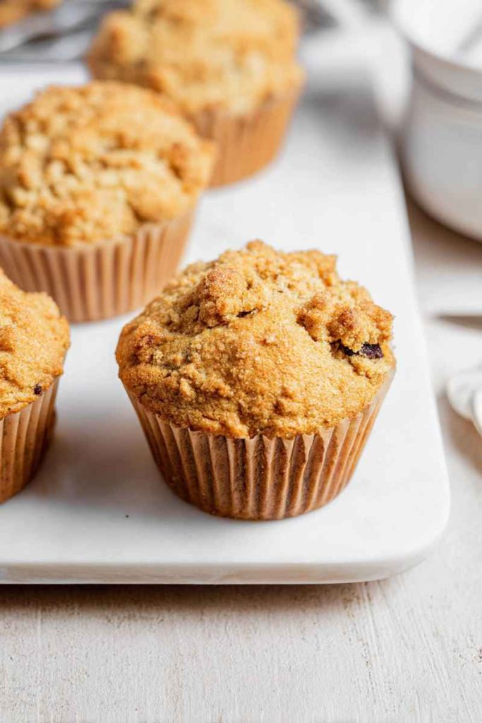 Three cappuccino muffins with streusel and chocolate on a white plate and wooden board.