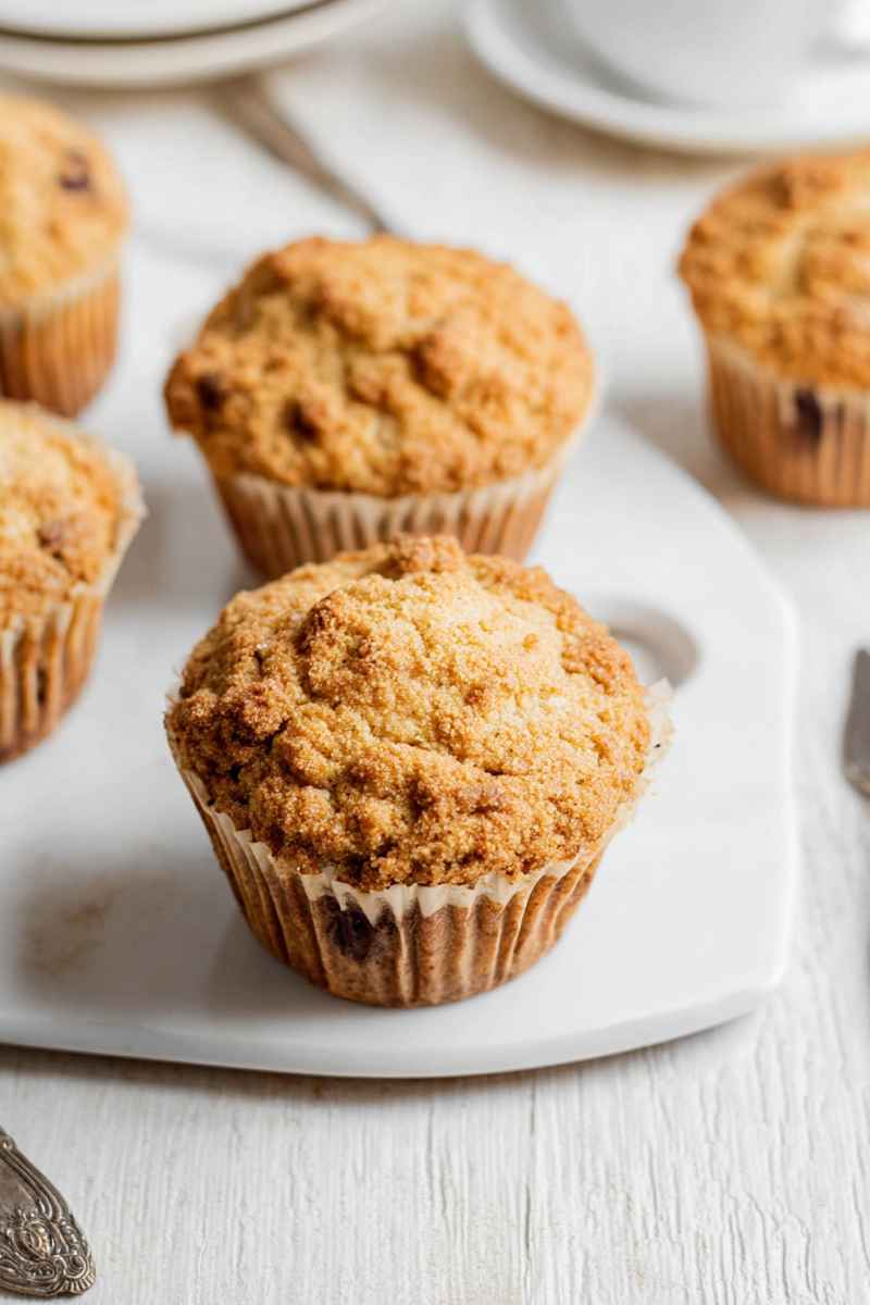 Group of four cappuccino muffins with streusel and chocolate chips on a white surface.
