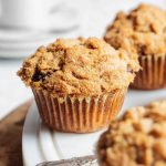 Close-up of a golden cappuccino muffin with chocolate chips and streusel on a white plate.