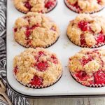A tray of golden-brown cherry cobbler muffins with visible streusel topping and bright red cherries.