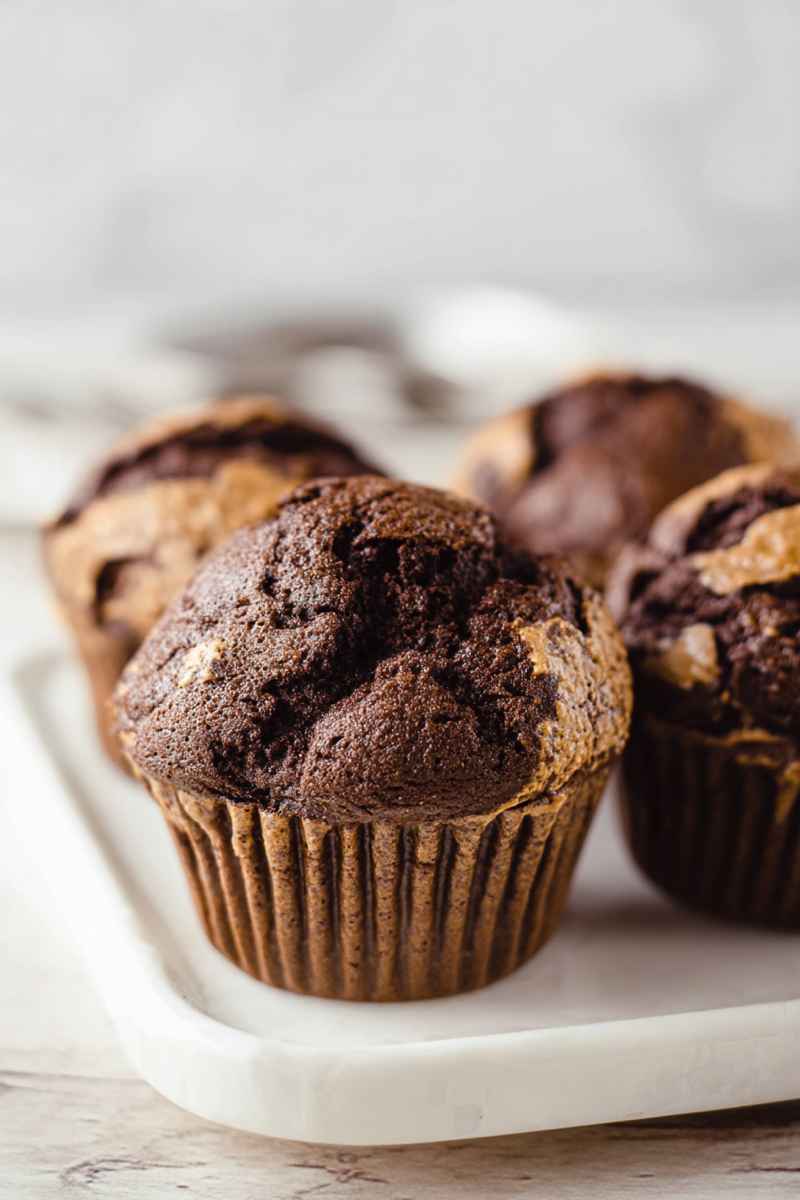 Chocolaty muffins with peanut butter swirls on a white serving tray.