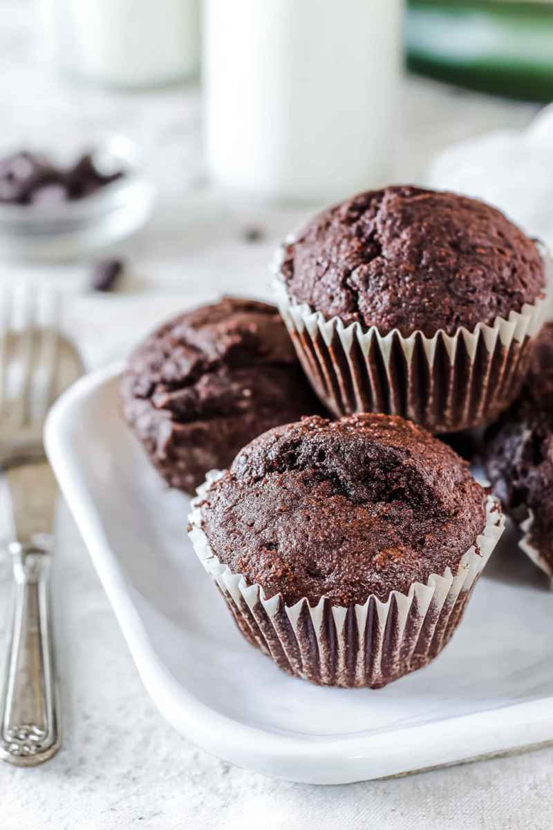 Stacked chocolate zucchini muffins on a white plate, emphasizing their homemade appeal.