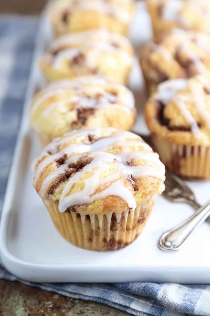 Close-up of glazed cinnamon swirl muffins in paper liners on a white plate with a blue checkered cloth.
