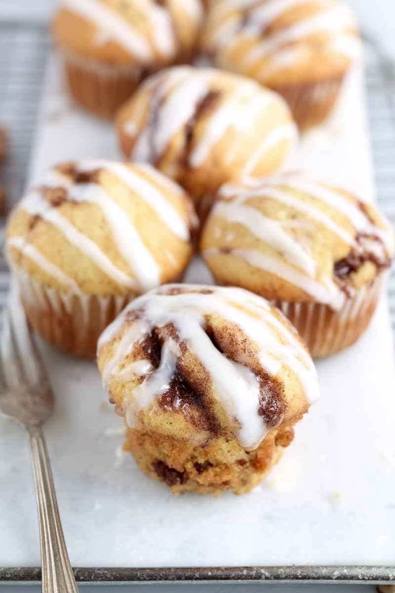 Several iced cinnamon muffins with streusel filling on a white marble surface with a vintage fork.