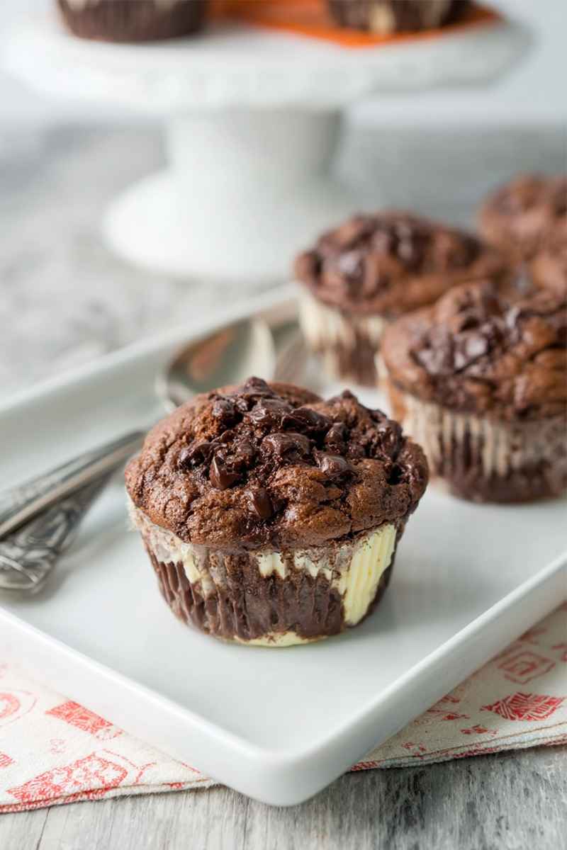 Chocolaty muffins topped with mini chocolate chips, showcasing a creamy cheesecake layer inside.