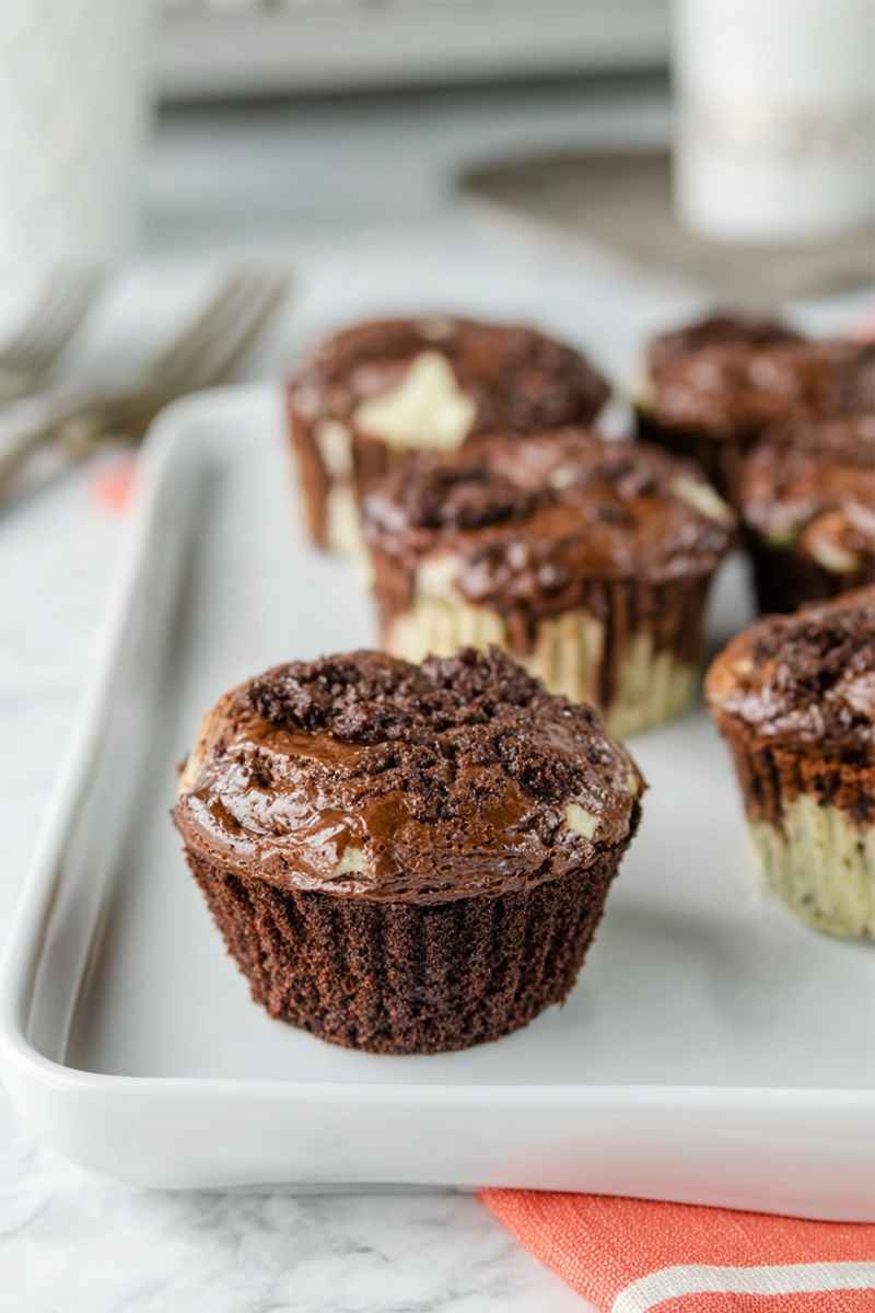 Rows of chocolate muffins with visible cheesecake layers, arranged on a white tray.