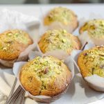 Golden pistachio muffins dusted with powdered sugar and garnished with chopped pistachios, displayed on a white plate.
