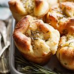 Close-up of Garlic Rosemary Focaccia Muffins with visible herb toppings and a golden, crispy crust, set against a rustic wooden background.