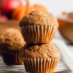 Pumpkin muffins dusted with sugar, placed on a cooling rack with vibrant pumpkins in the background.