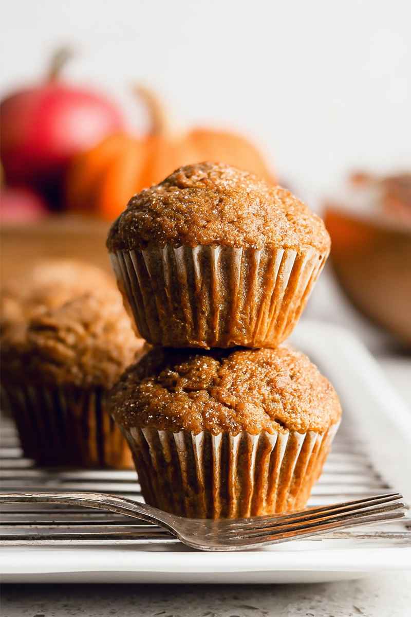Pumpkin muffins dusted with sugar, placed on a cooling rack with vibrant pumpkins in the background.