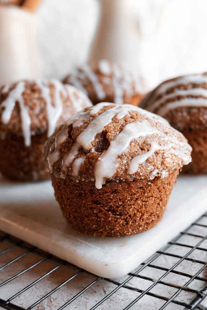 Group of frosted gingerbread muffins on a white marble surface and a wire rack, with a blurry background.