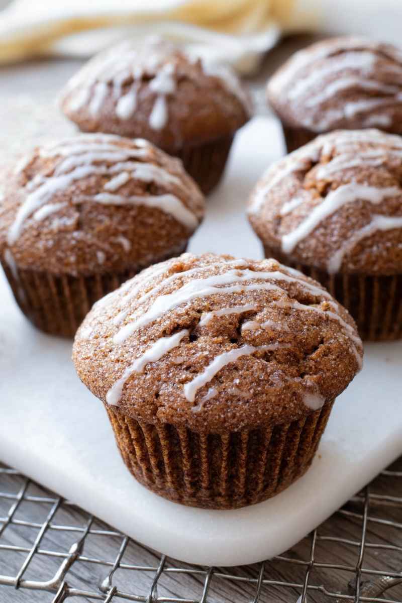 Several iced gingerbread muffins with visible coarse sugar, sitting on a white platter over a wire cooling rack.