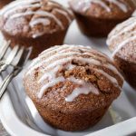 Close-up of several glazed gingerbread muffins on a white serving dish with a blurred wooden background.