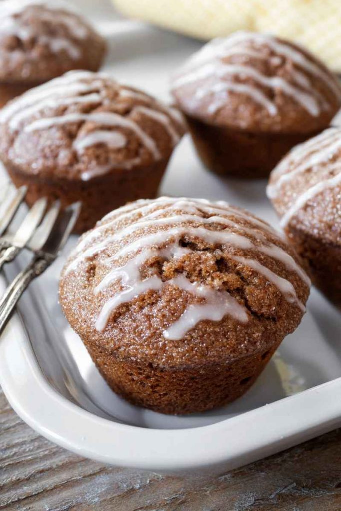 Close-up of several glazed gingerbread muffins on a white serving dish with a blurred wooden background.