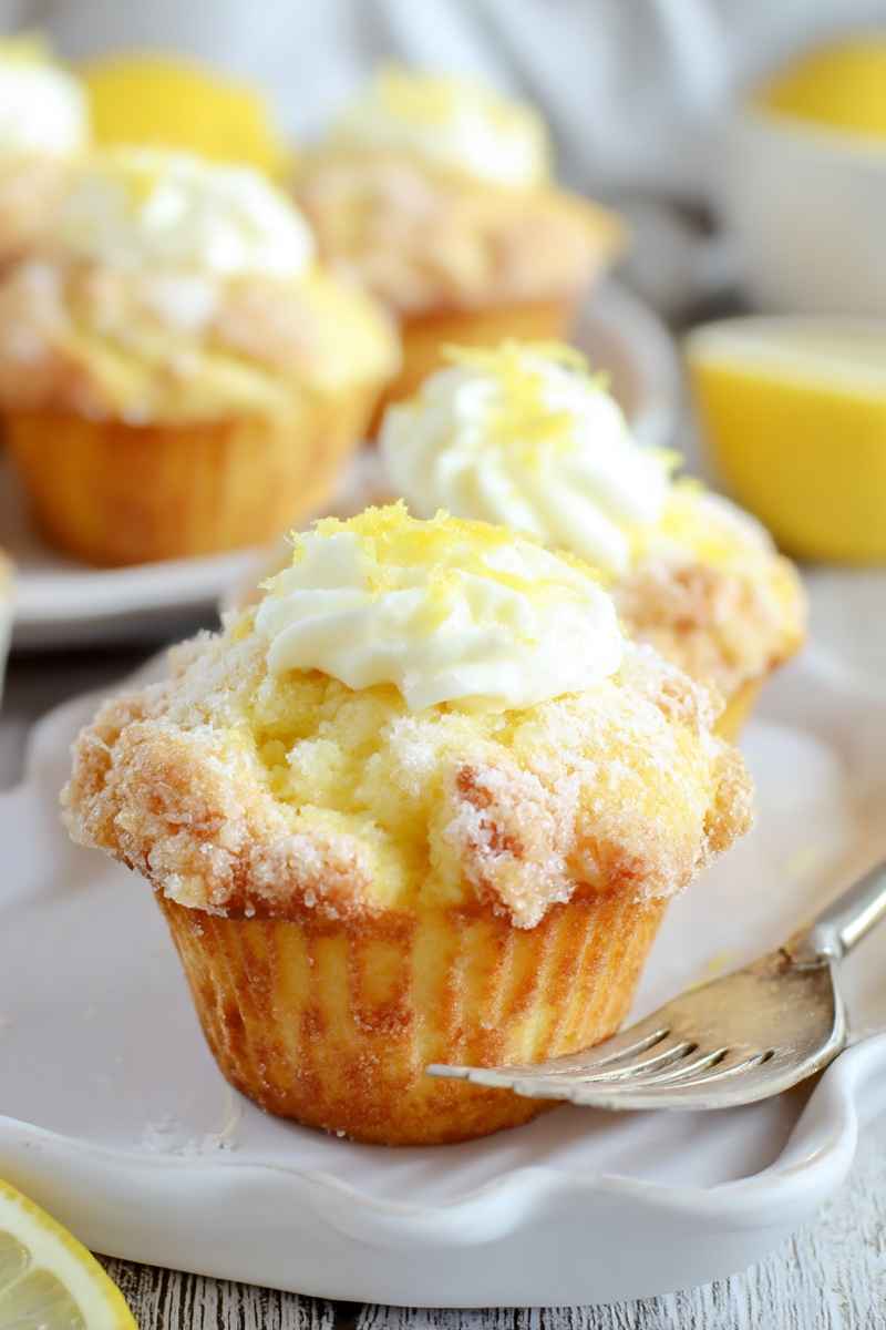 Golden-brown lemon muffins with a crumbly streusel topping and a dollop of whipped cream, garnished with lemon zest