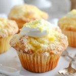 Close-up of a lemon muffin with a swirl of cream cheese frosting and sprinkled lemon zest, ready to be enjoyed.