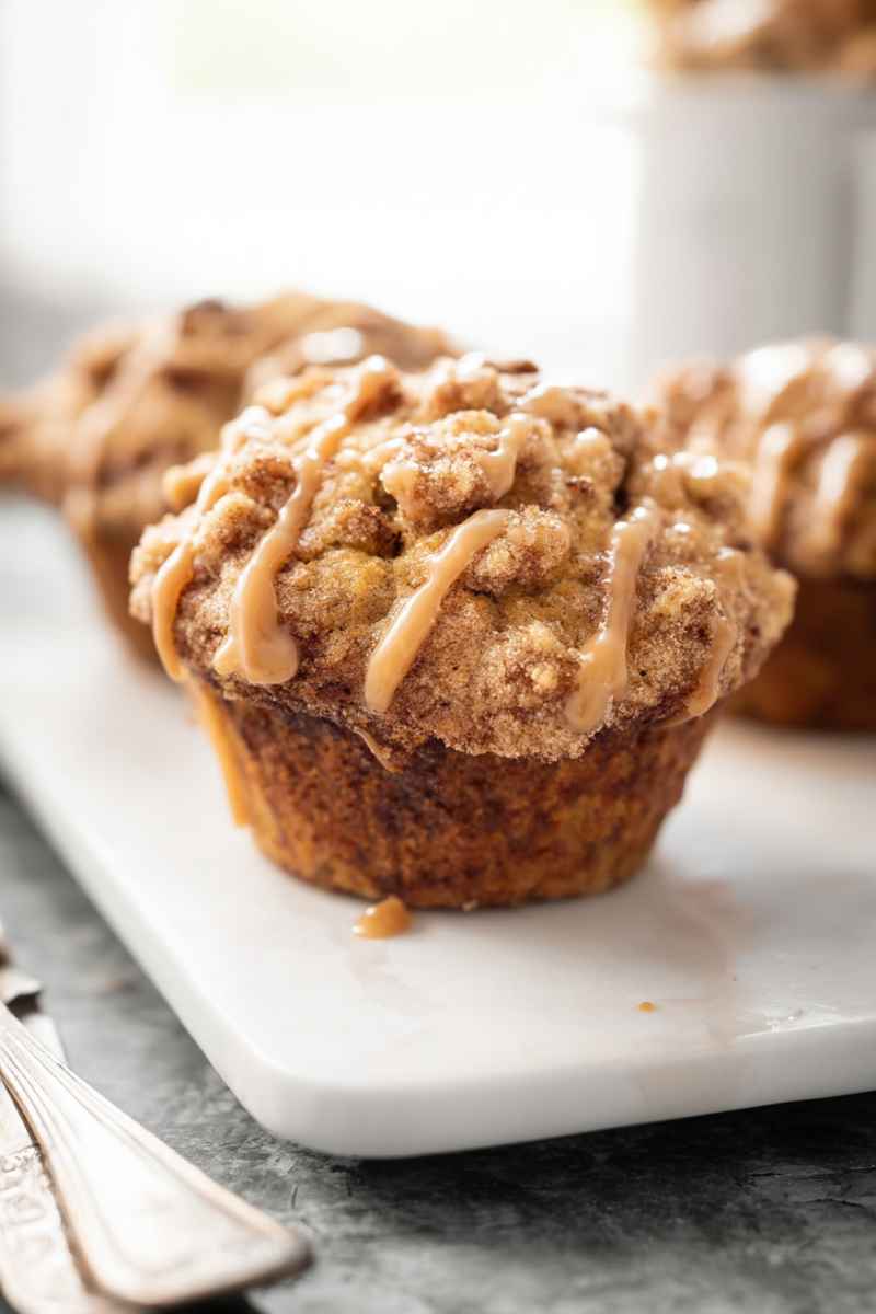 A beautifully presented Maple Walnut Muffin with a glossy maple glaze and crumbly streusel topping, placed on a white marble surface.