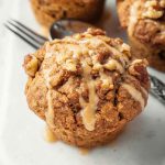 A close-up of a Maple Walnut Muffin with a golden-brown crust, crumbly streusel, and a shiny maple glaze, set against a rustic background.