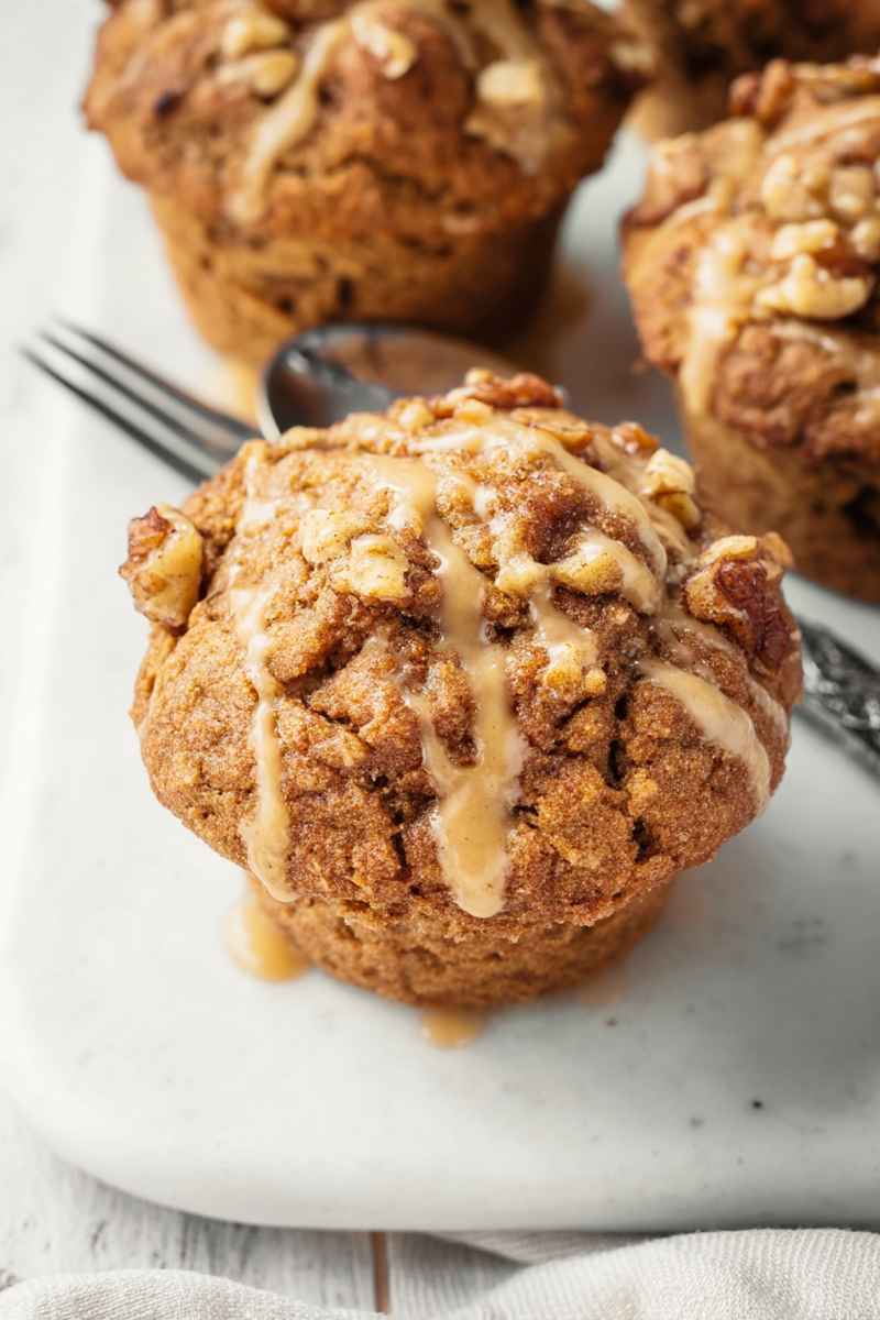 A close-up of a Maple Walnut Muffin with a golden-brown crust, crumbly streusel, and a shiny maple glaze, set against a rustic background.