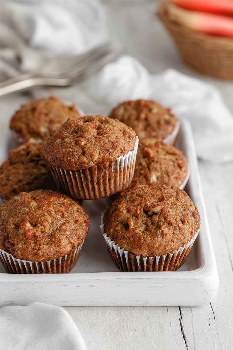 A tray of freshly baked carrot cake muffins with visible chunks of carrots and nuts, placed on a white surface.