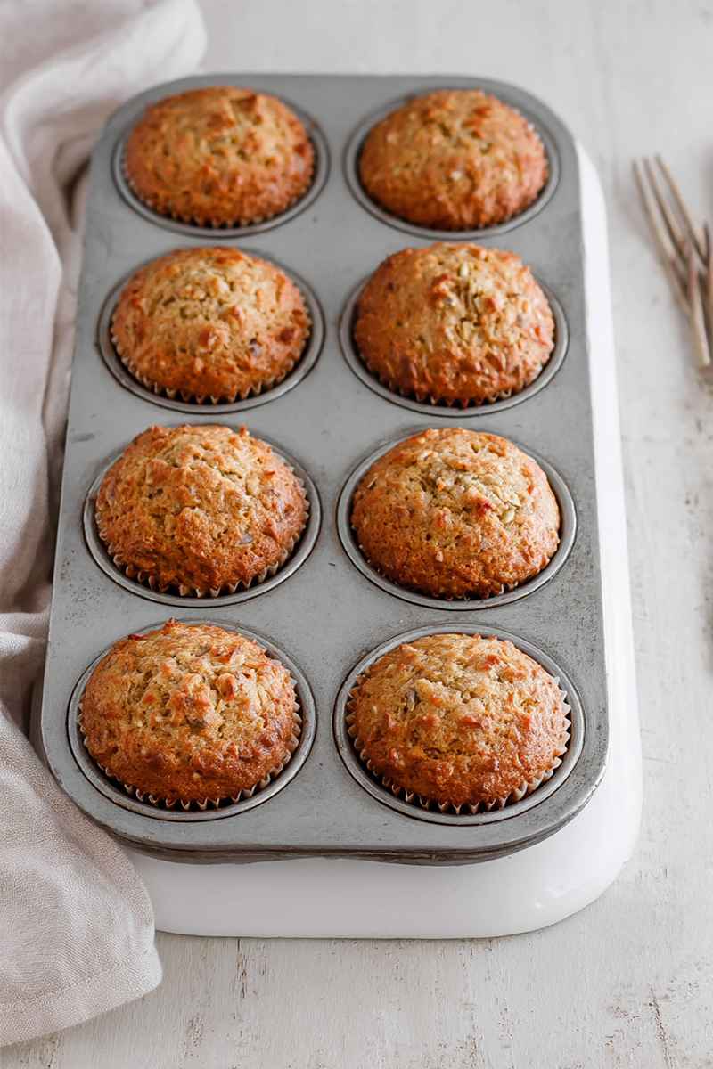 Six fluffy carrot muffins in a muffin tin, highlighting their golden-brown crust and soft texture.