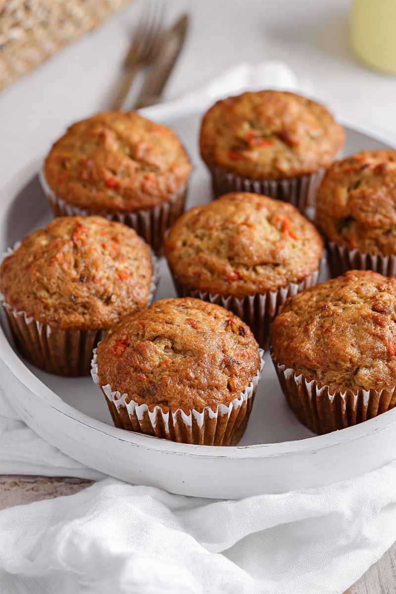 A close-up of golden-brown carrot muffins with visible carrot pieces, arranged neatly on a white plate.