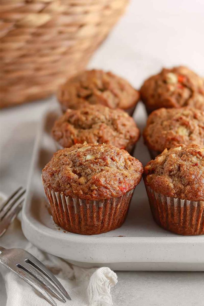 A cluster of carrot muffins with visible nut pieces, set on a rustic wooden table with a woven basket in the background.