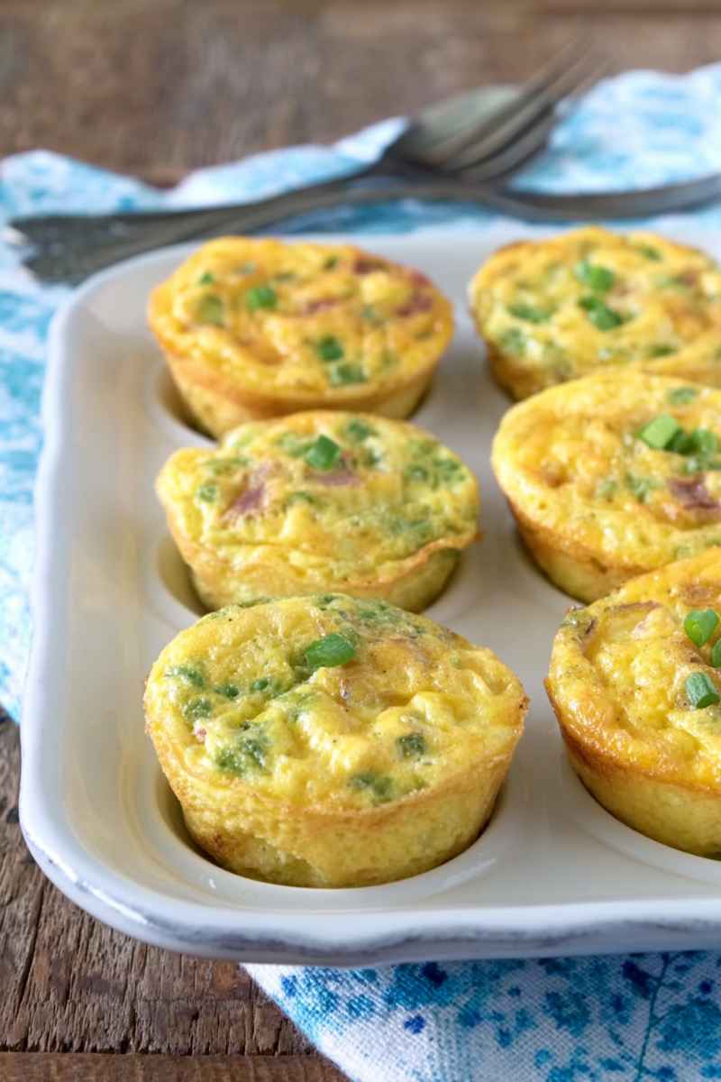 Golden-brown muffin tin omelets topped with fresh green onions, served on a white plate.