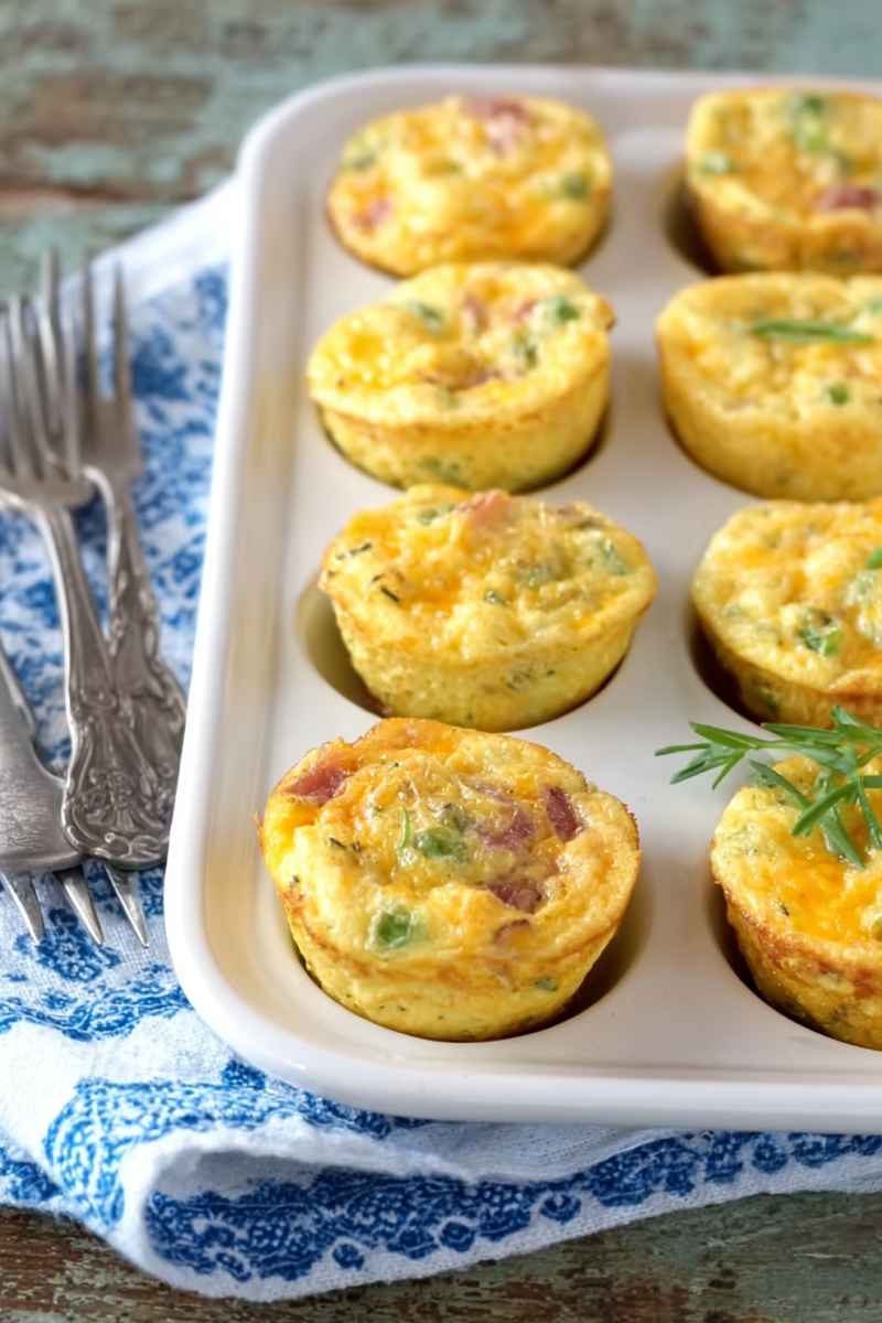Six golden muffin tin omelets garnished with fresh herbs, arranged neatly on a white tray.