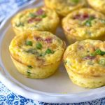 Six golden muffin tin omelets topped with green onions, presented on a decorative blue-and-white plate.