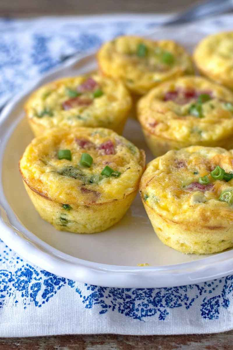 Six golden muffin tin omelets topped with green onions, presented on a decorative blue-and-white plate.