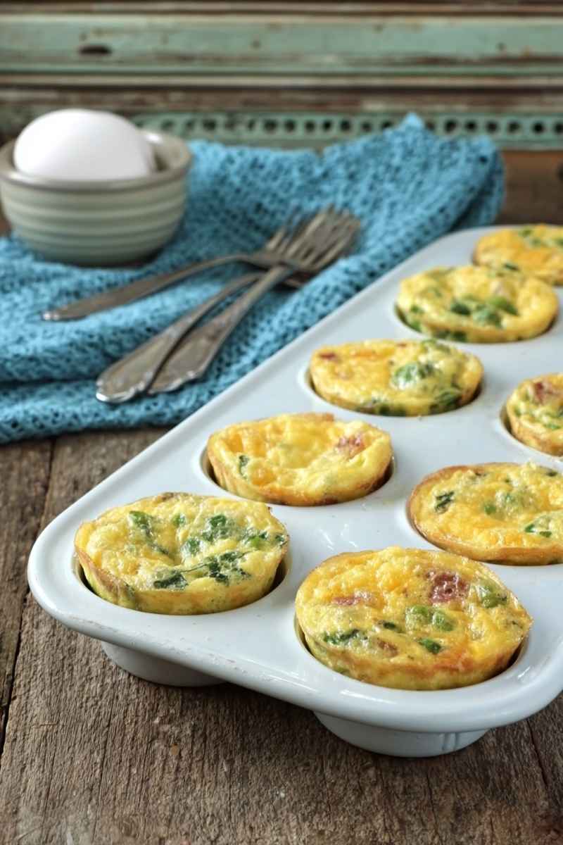 Muffin tin omelets filled with cheese and sausage, garnished with fresh herbs, displayed on a rustic wooden table.