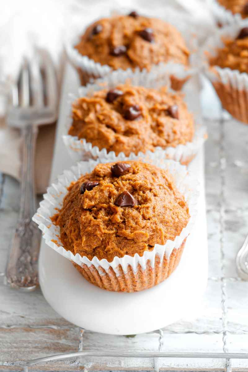 Row of Paleo Sweet Potato Muffins with chocolate chips, placed on a white plate with vintage forks nearby.