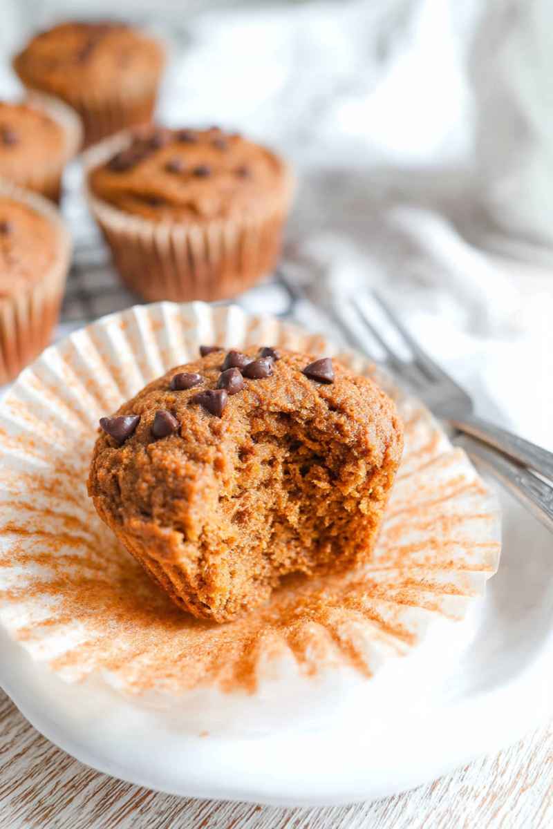 A partially eaten Paleo Sweet Potato Muffin revealing its moist interior, surrounded by whole muffins.