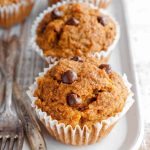 Three Paleo Sweet Potato Muffins with chocolate chips, arranged on a white plate with antique forks.