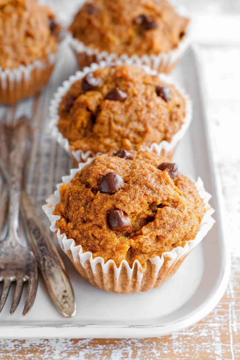 Three Paleo Sweet Potato Muffins with chocolate chips, arranged on a white plate with antique forks.