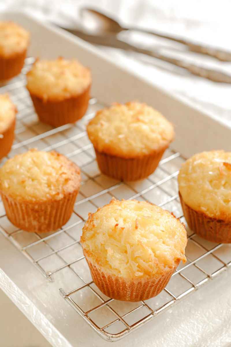 Freshly baked Pina Colada muffins cooling on a wire rack, topped with coconut flakes.