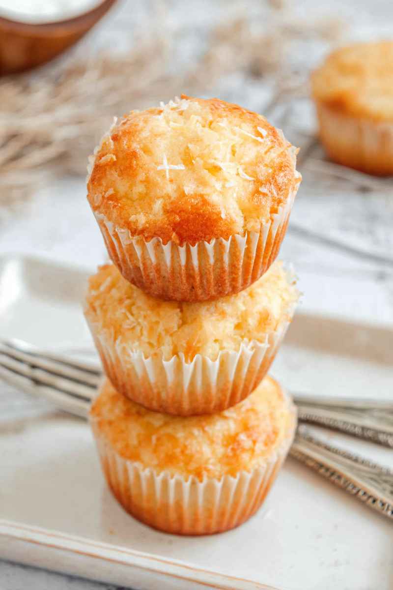 Three golden Pina Colada muffins stacked on top of each other, showcasing their fluffy texture and coconut topping.