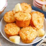 A plate of golden Pina Colada muffins garnished with fresh pineapple slices and coconut flakes.
