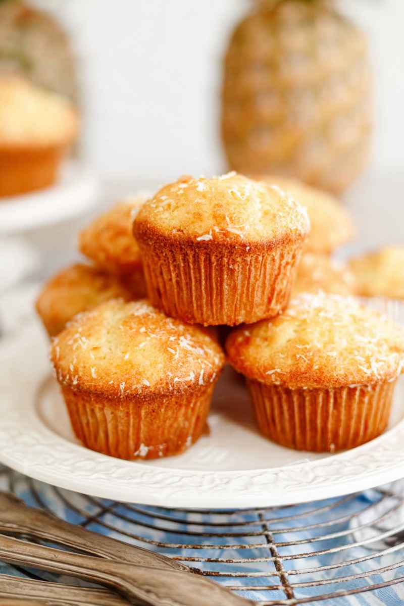 A stack of golden Pina Colada muffins garnished with coconut flakes, served on a decorative white plate.
