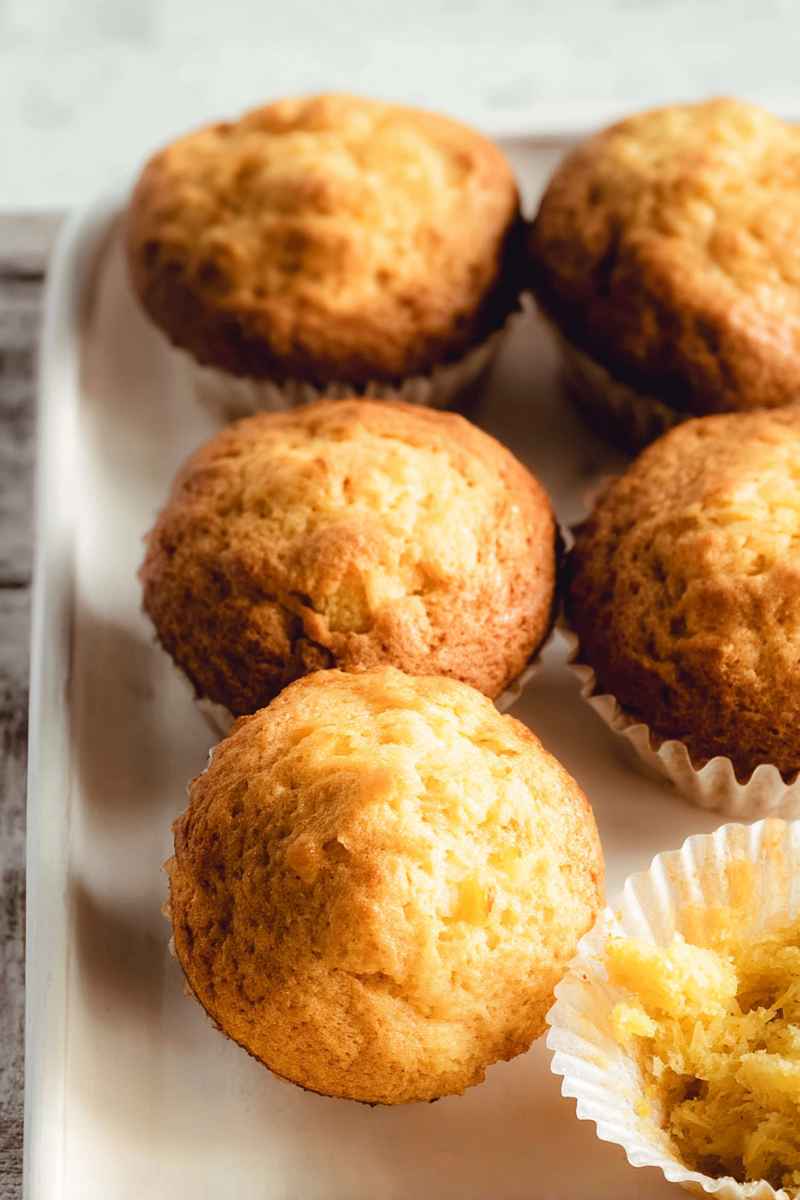 A close-up of golden pineapple muffins arranged on a white tray, showcasing their tender texture.