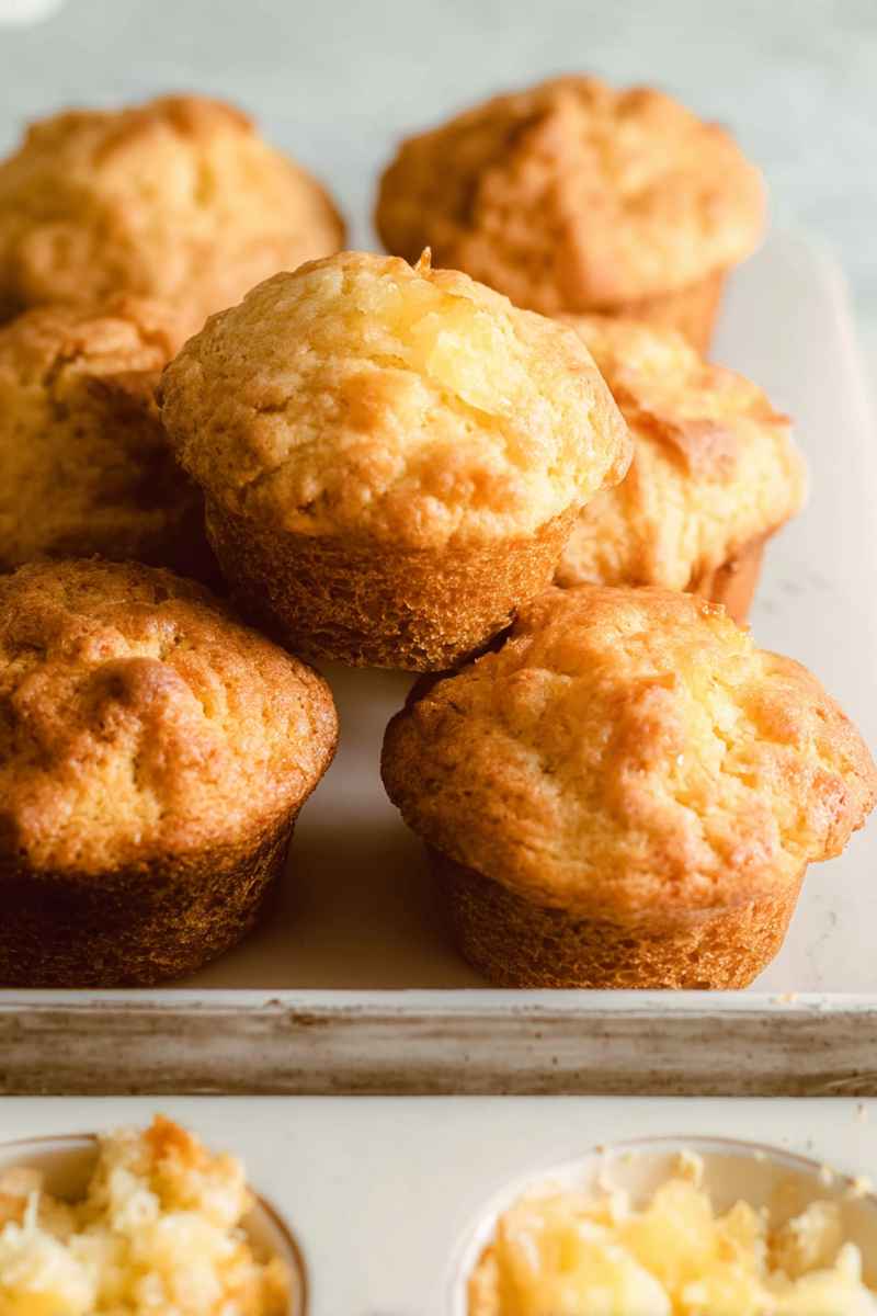 A stack of golden pineapple muffins on a rustic wooden surface, highlighting their warm, inviting appearance.