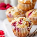 A close-up of a White Chocolate Raspberry Muffin with drizzled white chocolate glaze.